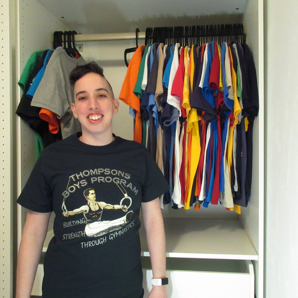 Katelyn standing in front of hanging t-shirts wearing a green t-shirt.
